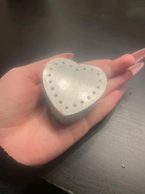 Hjärformad smyckesask i metall - Söt hjärtformad smyckesask i silverfärgad metall med små glittrande stenar runt locket. Perfekt för att förvara ringar, örhängen eller andra småsaker. Insidan är klädd i mörkblått tyg för extra lyxig känsla. Enkel och stilren design som passar på sminkbordet.