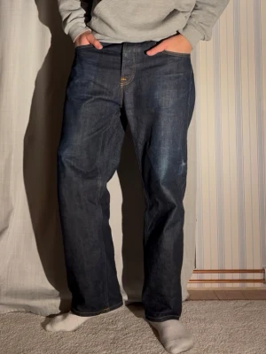 Nudie selvage denim jeans - Säljer ett par mörkblå selvege denim jeans från nudie modell tuff Tony. Storlek 33/30 men sitter mer som 32/32. Modellen är 188 lång väger 78kg. Total längd 102, benöppning 22 midja 43