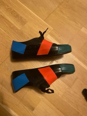 Melissa crew - Unika sneakers i svart med snörning, dekorerade med breda färgblock i blått, rött och grönt. Skorna har en låg profil och är tillverkade i ett glansigt syntetmaterial. Perfekt för dig som gillar att sticka ut med din stil.