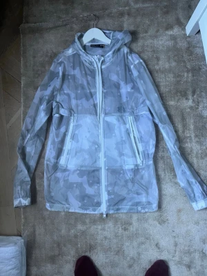 Under armor windbreaker - Grå windbreaker från under armor i storlek M. Coolt camoflauge mönster. Skriv vid minsta fundering!