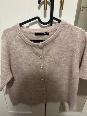 Ljusrosa kofta med pärlknappar - Supersöt ljusrosa kofta från lager 157 kort ärm och rund halsringning. Koftan har pärlknappar framtill och är stickad i ett mjukt material. Perfekt att slänga över en topp för en söt look.