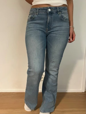 Ljusblå bootcut jeans - Säljer ett par ljusblå bootcut jeans med hög midja och klassisk femficksmodell. Jeansen har en snygg tvätt och raka ben som går ut lite nedtill. Perfekta till en avslappnad och trendig look. Materialet är mjukt denim i bomull.