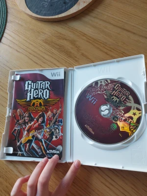 Guitar Hero Aerosmith till Wii - Guitar Hero Aerosmith till Nintendo Wii, komplett med fodral och manual. Omslaget har färgstark grafik med Aerosmiths logga och bandmedlemmar. Spelet är på skiva och passar för dig som gillar musikspel och rock. Perfekt för spelkvällar med vänner!