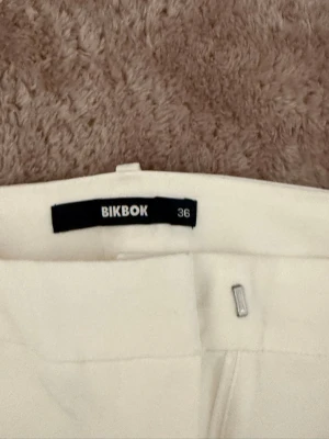 Vita kostymbyxor från BikBok - Säljer ett par stilrena vita kostymbyxor från BikBok i storlek 36 petite. Low waist, finns ett litet fläck men syns inte 