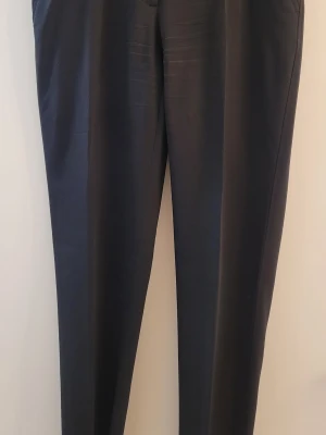 Svarta kostymbyxor Dolce & Gabbana - Snygga svarta kostymbyxor från Dolce & Gabbana, tillverkade i Italien. Byxorna har klassisk rak passform, pressveck och är gjorda i 98% ull och 2% elastan för en skön stretch. Perfekta för en stilren och elegant look.