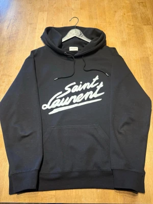 Svart Saint Laurent hoodie  - Snygg Saint Laurent hoodie i storlek M, men den skulle passa någon som bär storlek S bättre. Tröjan är nästan i väldigt bra skick och endast använd ett fåtal gånger. Tveka inte att skriva för fler bilder eller om du undrar något! Mvh Felkannn