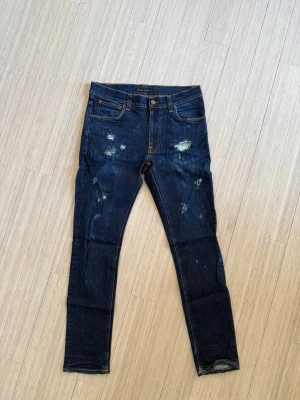 Mörkblå slitna Nudie jeans - Mörkblå slimfit jeans med slitningar och hål på framsidan. Jeansen har högre midja, slitningar och sitter som slimfit. Vid fler frågor eller intresse för fler bilder är det bara att höra av sig🤠