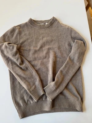 Beige stickad tröja med rund hals - Säljer en enkel och stilren beige stickad tröja från Dobber med rund halsringning och ribbade muddar vid ärmslut och nederkant. Skriv ifall du har några frågor!