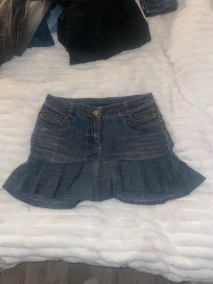 Jeanskjol med volang från KappAhl - Säljer en snygg blå jeanskjol från KappAhl med volangkant nedtill. Kjolen har klassiska fickor fram och bak, knapp och dragkedja i midjan. Perfekt för dig som gillar denim och vill ha en cool, avslappnad stil.