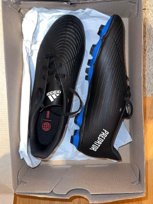 Adidas Predator Svarta Fotbollsskor - Snygga svarta Adidas Predator fotbollsskor med blå sula och vita detaljer. Storlek 42, passar även 41.  Pris 399kr + frakt. Aldrig använt. 