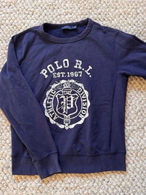 Mörkblå sweatshirt från Polo Ralph Lauren🙌🤩 - Säljer en mörkblå sweatshirt från Polo Ralph Lauren med vit tryckt logga och text 'POLO R.L. EST. 1967' på bröstet. Tröjan har rund halsringning, långa ärmar och ribbade muddar. Perfekt för en avslappnad och sportig stil.🙌🤩