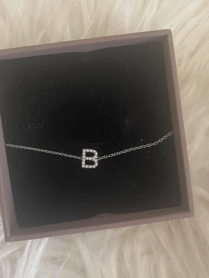 Silverarmband med bokstaven B - Snyggt och stilrent armband i silverfärg med en tunn kedja och ett hänge i form av bokstaven B. Bokstaven är dekorerad med små glittrande stenar som ger en exklusiv känsla. Perfekt för dig som vill ha något personligt och trendigt. Nypris 349kr (kolla hemsidan för stormen, denna är i S)