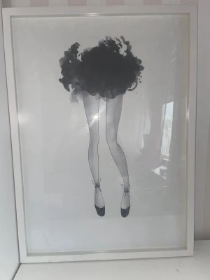 Stilren tavla med ballerina-motiv - Säljer en tavla med en konstnärlig illustration av en ballerina i svart och vitt. Motivet visar ben i ballerinaskor och en abstrakt kjol, inramad i vit ram. Perfekt som dekoration i sovrum eller vardagsrum.