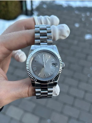 Silverfärgad klocka med romerskasiffror - Stilren klocka i silverfärgat metallarmband och boett. Urtavlan är också silver med romerska siffror, kommer med förstorings länkar.