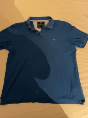 Blå pikétröja från Paul & Shark - Snygg blå pikétröja från Paul & Shark med klassisk krage och knappar framtill. Tröjan har korta ärmar och är tillverkad i mjuk bomull. Liten logga broderad på bröstet för en clean look.