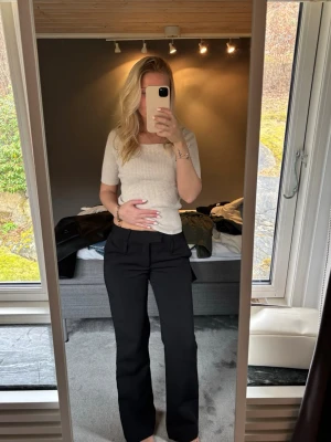 Svarta kostymbyxor med raka ben - Snygga svarta kostymbyxor med raka ben och hög midja. Klassisk passform som ger en clean och stilren look. Perfekta till både skjorta och t-shirt. Byxorna har diskreta fickor i sidorna och stängs med dragkedja och knapp.