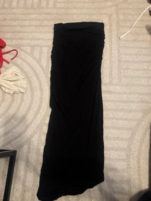 Svart långkjol i mjukt tyg - En svart långkjol med rak passform. Kjolen är enkel och stilren utan synliga detaljer eller mönster. Materialet känns mjukt och lätt och ha Ingen synlig logga eller märke.