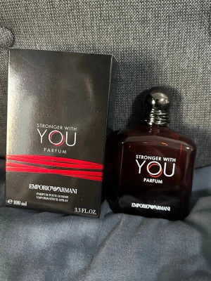 Emporio Armani Stronger With You Parfum - Emporio Armani Stronger With You Parfum är en elegant herrdoft i en mörkbrun, fyrkantig glasflaska med rundad svart kork. Flaskan har vit och röd text och kommer i en matchande svart kartong med röda detaljer. Volymen är 100 ml.