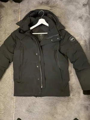 Black Label Canada goose wyndham  - Säljer en svart dunjacka från Canada Goose Black label med avtagbar huva och pälsdetalj. Jackan har två sidofickor med dragkedja, hög krage och logotyp på ärmen. Perfekt för kalla vinterdagar och riktigt varm tack vare dunfyllningen. Jackan är i mycket bra skick och är väldigt få använd. 