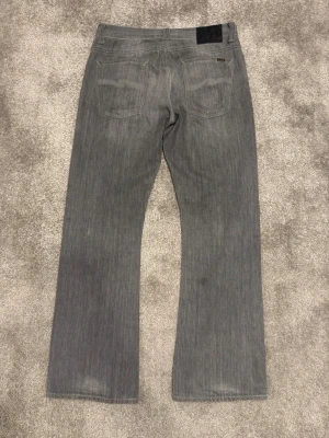 Nudie Jeans Regular Alf - Säljer ett par grå jeans från Nudie Jeans med rak passform och klassisk femficksdesign. Jeansen har subtila slitningar och är tillverkade i ett mjukt denimtyg. Perfekta för en avslappnad och stilren look. Model Regular Alf.                                                    Längd:106 cm Midja:44 cm Benöppning:26 cm