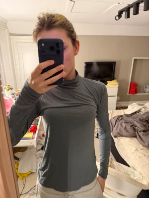 Grön polotröja med långa ärmar - Säljer en enkel och stilren grön polotröja med långa ärmar. Tröjan har en tight passform och är tillverkad i ett mjukt, stretchigt material som sitter skönt mot kroppen. Perfekt att matcha med jeans eller kjol för en clean look.