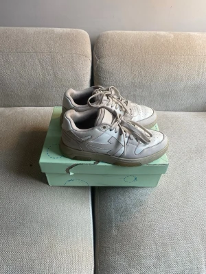 Vita Off-White out of office sneakers - Säljer ett par vita Off-White sneakers med den ikoniska pil-loggan på sidan. Skorna har perforerad tå, tjock sula och klassiska Off-White skosnören med text. Tillverkade i läder och mesh för en clean och modern look. Nypris 660 dollar.