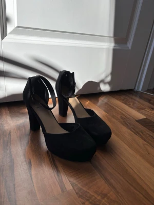 Svarta chunky pumps med ankelrem -  svarta pumps med chunky klack och rundad tå. Skorna har en bred ankelrem med spänne och är tillverkade i mockaimitation. Skorna har tecken på användning (se sista bilden) 