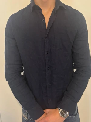 Mörkblå Linneskjorta  - Snygg mörkblå linneskjorta från dressmann med klassisk krage och knappar framtill. Tillverkad i linne för en luftig och avslappnad känsla. Skjortan har lång ärm och en stilren, tidlös look som passar till jeans eller chinos. Perfekr på sommaren