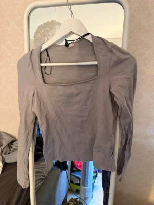 Ljusgrå långärmad topp Gina Tricot - Säljer en ljusgrå långärmad topp från Gina Tricot med fyrkantig urringning. Toppen är tight i modellen och tillverkad i mjuk bomullsmix, perfekt att styla med jeans eller kjol. Enkel och stilren design som passar till det mesta.