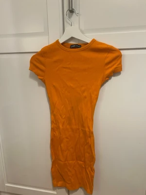 Orange ribbad kortklänning - Kort, ribbad klänning i stark orange från PrettyLittleThing. Modellen är figurnära med rund halsringning och korta ärmar. Perfekt för dig som vill ha en enkel men färgstark look.