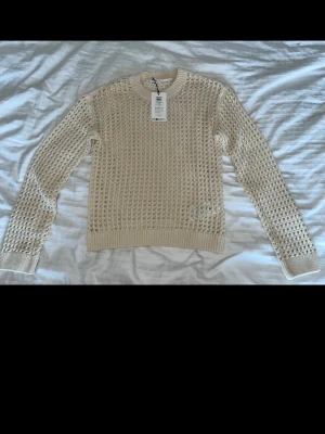 Beige stickad tröja  - Helt ny stickad tröja från Object med hålmönster och rund halsringning. Tröjan har långa ärmar och ribbade muddar vid ärmslut och nederkant. Perfekt för lager på lager och ger en cool, avslappnad vibe.