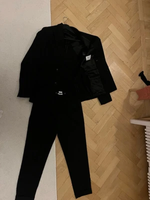 Svart kostym från Filipa K med dubbelknäppt kavaj - Stilren svart kostym från Filipa K med dubbelknäppt kavaj och byxor. Klassisk passform och tidlös design, perfekt för dig som vill ha en clean och elegant look. Kavajen har breda och tidlösa  slag. Materialet känns mjukt och följsamt. Köpt för över 5000 kr för ca 10 månader sen i Stockholm och sparsamt använd. Storlek 46 på kavaj och byxa 