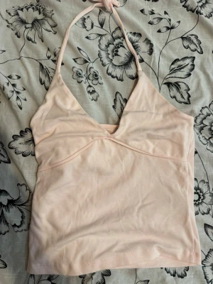 Ljusrosa halterneck linnetopp - Säljer en ljusrosa halterneck linnetopp med v-ringad front och knyt i nacken. Toppen är ärmlös och har en enkel, stilren design som passar perfekt till sommaren. Tillverkad i mjukt bomullsmaterial för en bekväm känsla.