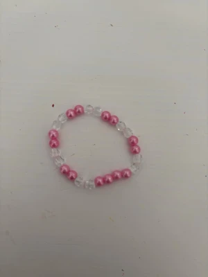 Rosa och transparent pärlarmband - Sött armband med rosa och transparenta pärlor i plast. Armbandet är elastiskt och har ett enkelt men trendigt utseende som passar perfekt till din vardagsstil. Perfekt accessoar för dig som gillar färg och lekfulla detaljer.