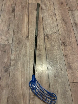Unihoc innebandyklubba UNISLIM 29 - Säljer en svart innebandyklubba från Unihoc, modell UNISLIM 29. Klubban har ett blått blad och grått grepp. Perfekt för dig som gillar innebandy och vill ha en lätt och smidig klubba med snygg design. Har en Zorro hook på men går lätt att byta