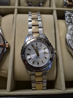 Dyrberg - Stilren klocka från Danish Design med länkarmband i silver och guld. Urtavlan är vit med guldfärgade markeringar och datumvisning. Klassisk rund form och elegant design som passar till många stilar.