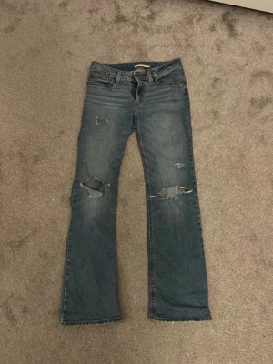 Levi's blå slitna bootcut jeans - Säljer ett par Lågmidjade blå Levi's jeans med bootcut och slitningar då de tyvärr inte passar mig. Innerbenslängd: ca 79cm, och Midjebredd tvärs över är ca 37💕 lite stretchiga är dom också! Skriv privat för Bilder osv. Köpta second hand därav lite slitningar längst ner men aldrig använda av mig🤗