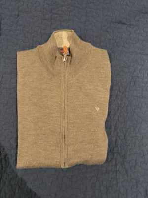 beige ziptröja från Morris - Snygg beige ziptröja från Morris med hög krage och diskret broderad logga på bröstet. Tröjan har hel dragkedja, ribbade muddar och är tillverkad i mjukt stickat material. Perfekt för lager på lager och enkel att matcha.