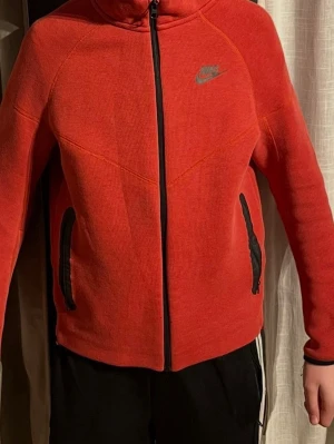 Röd Nike tech fleece hoodie - Skriv vid minsta lilla fråga!!!!! Snygg röd hoodie från Nike med hel dragkedja framtill och två svarta fickor med dragkedja. Hoodien har en klassisk Nike-logga på bröstet och en skön huva. Perfekt för chill eller träning. Materialet känns mjukt och bekvämt.
