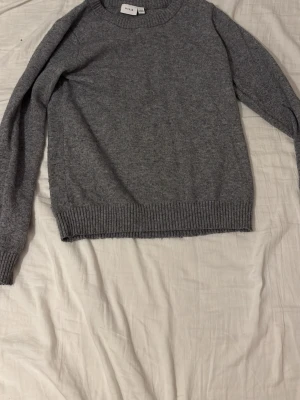 Grå stickad tröja från Vila - Mysig grå stickad tröja från Vila med rund halsringning och ribbade muddar vid ärmslut och nederkant. 