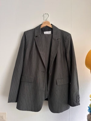 Set kavaj +byxor från Bubbleroom - Snygg grå kavaj från Bubbleroom med tunna vita kritstrecksränder. Klassisk passform med två fickor fram, knäppning och tre knappar vid ärmslut. Perfekt för en stilren och trendig look. Setet säljs även separat på begäran! Priset gäller endast för kavajen, byxorna köps separat 