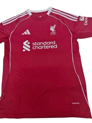 Liverpool matchtröja 25/26 hemma - Snygg röd Liverpool matchtröja från Adidas med vita detaljer och tryck. Framsidan har klubbmärke, Adidas-logga och sponsortryck. Baksidan har namnet Wirtz och nummer 7 i vitt. Tillverkad i lätt och ventilerande material, perfekt för fotboll eller träning.