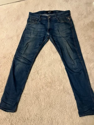 Blå slim fit jeans Replay - Snygga blå slim fit jeans från Replay med klassisk style och diskreta slitningar. Jeansen har dragkedjegylf. Tillverkade i stretchigt denim för extra komfort och en modern look. Använda jeans med skön passform/ storlek 31/30 modell: Anbass