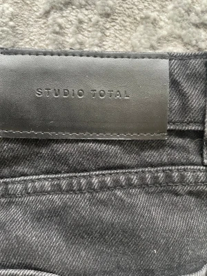 Svarta raka jeans från Studio Total - Snygga svarta jeans från Studio Total med klassisk femficksmodell och raka ben. Jeansen har normal midja och är tillverkade i ett mjukt denimtyg som ger en avslappnad men stilren look. Perfekta till en streetwear-outfit eller för en enkel vardagsstil. ( osäker på storlek) 