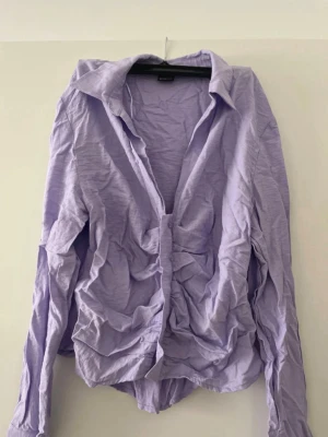 Ljuslila skjorta med knappar - Säljer en ljuslila skjorta med klassisk krage och knäppning framtill. Skjortan har lång ärm och är tillverkad i ett mjukt, tunt tyg som känns skönt mot huden. Perfekt för dig som gillar en enkel men snygg look.