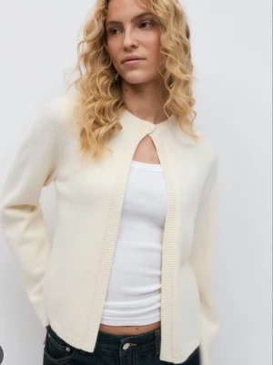 Krämvit cardigan med knapp - Stilren krämvit cardigan med rund halsringning och en dekorativ knapp upptill. Koftan har långa ärmar och ribbade kanter, perfekt att slänga över ett linne eller t-shirt. Enkel och clean design som passar till det mesta. Endast använd ett fåtal gånger!