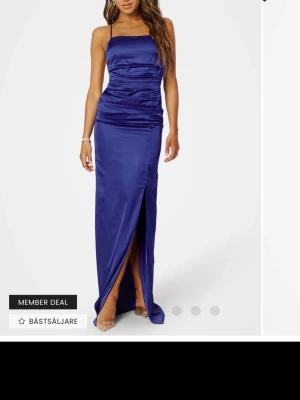 Blå långklänning med slits och smala band - Säljer min balklänning! Snygg blå långklänning i satinliknande material med smala axelband och öppen rygg med snörning. Klänningen har en figurnära passform och en hög slits framtill som ger en elegant look. Perfekt för bal. Har tecken på användning🫶🥰