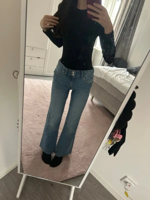 Blåa bootcut jeans med hög midja - Säljer ett par ljusblå bootcut jeans med hög midja och klassiska fem fickor. Jeansen har en avslappnad passform över låren och utsvängda ben. Tillverkade i denim med snygga söm-detaljer och knappgylf framtill. Pris går att diskutera 💕
