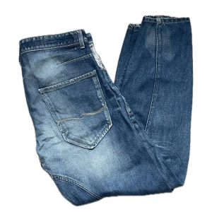 Blå raka jeans med slitningar - Säljer ett par klassiska blå jeans med raka ben och snygga slitningar. Jeansen har fem fickor, normal midja och en avslappnad passform. Perfekta för en casual look och tillverkade i slitstarkt denimtyg.