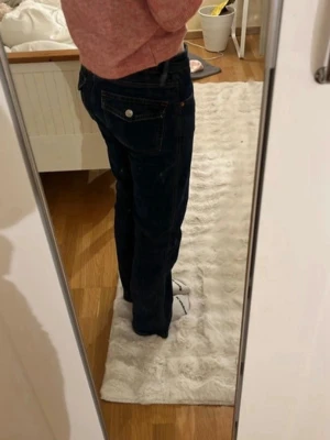 Mörkblå bootcut jeans med kontrastsömmar - Säljer ett par mörkblå bootcut jeans med kontrastsömmar och klassiska fem fickor. Jeansen har en låg midja och stängs med knapp och dragkedja. Snygga detaljer med nitar och ficklock bak. Perfekta till en avslappnad stil.